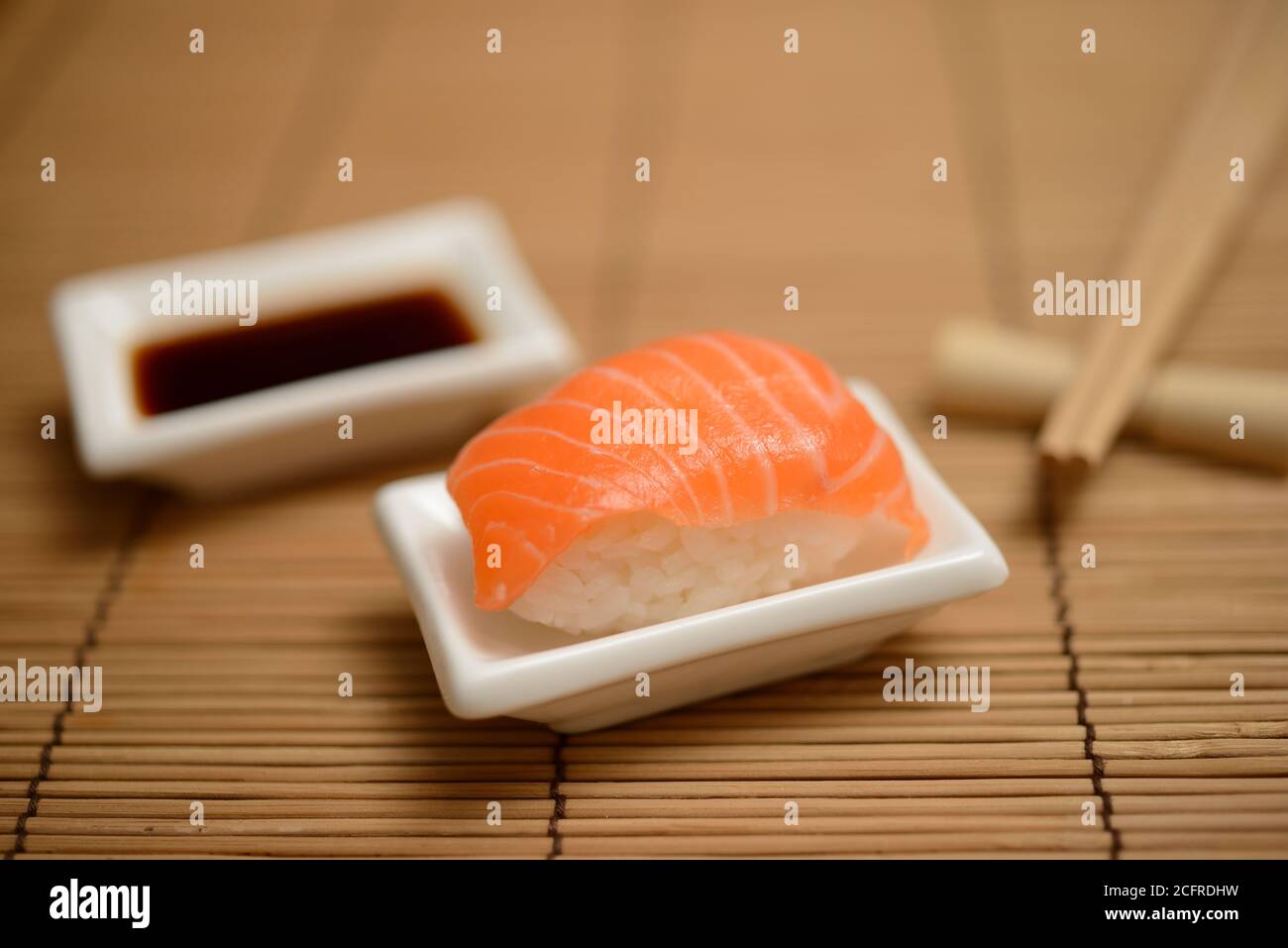 Essstäbchen, Sojasauce und Sushi mit Lachs auf der Bambusmatte Stockfoto