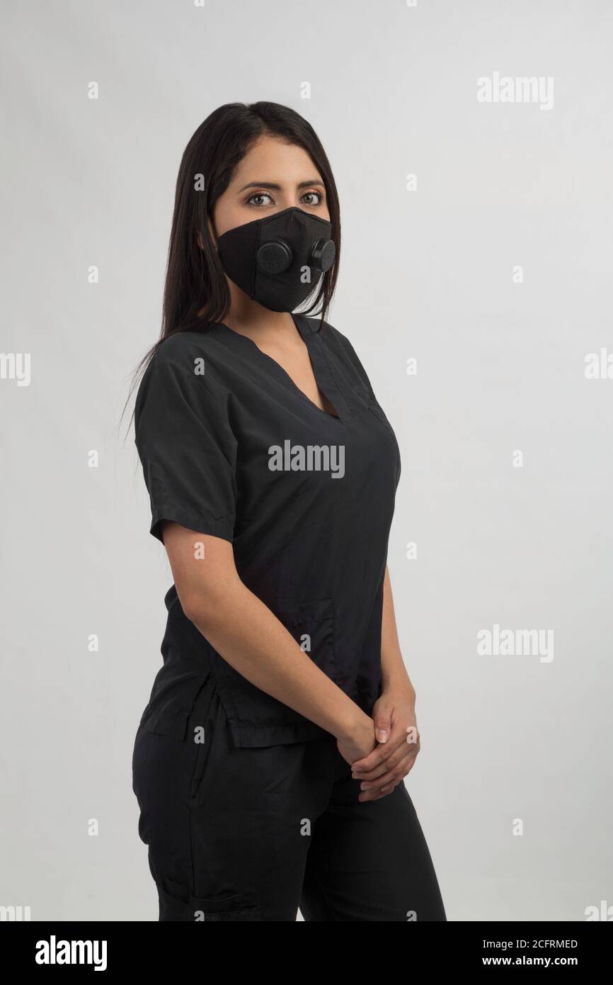 Schönheit Krankenschwester in schwarz mit Maske gekleidet, stehend im Studio mit grauem Hintergrund Stockfoto