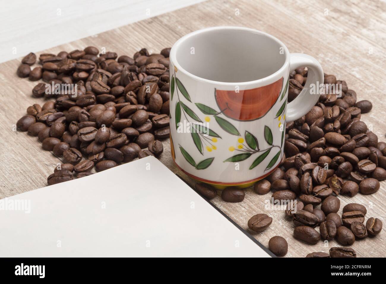 Detail einer Tasse mit Kaffeebohnen neben einem Buch, auf einem Holztisch, Studio Stockfoto
