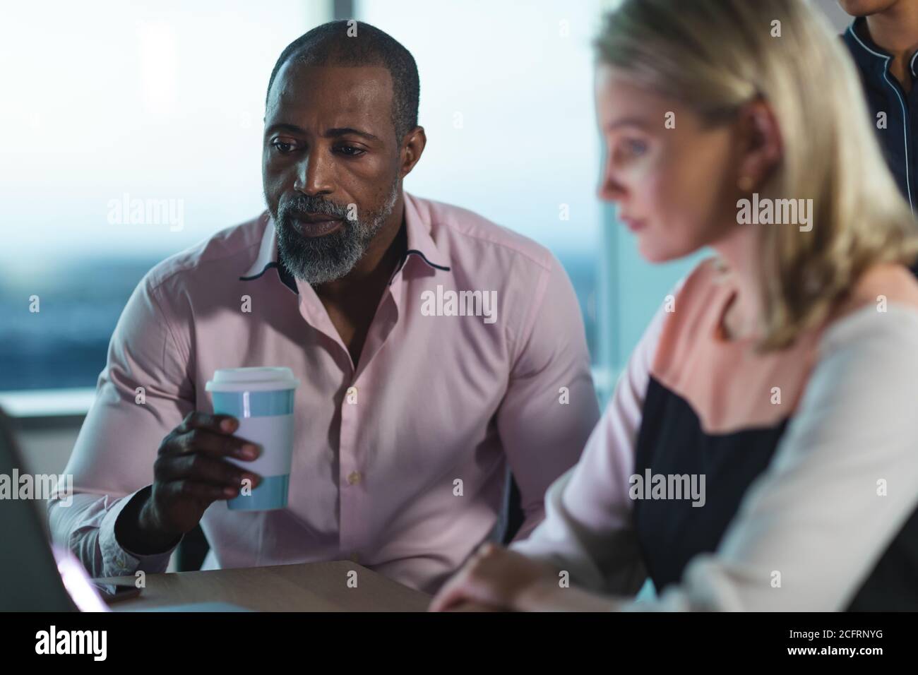 Senior Geschäftsmann trinkt Kaffee, während junge Geschäftsfrau mit Laptop an Modernes Büro Stockfoto