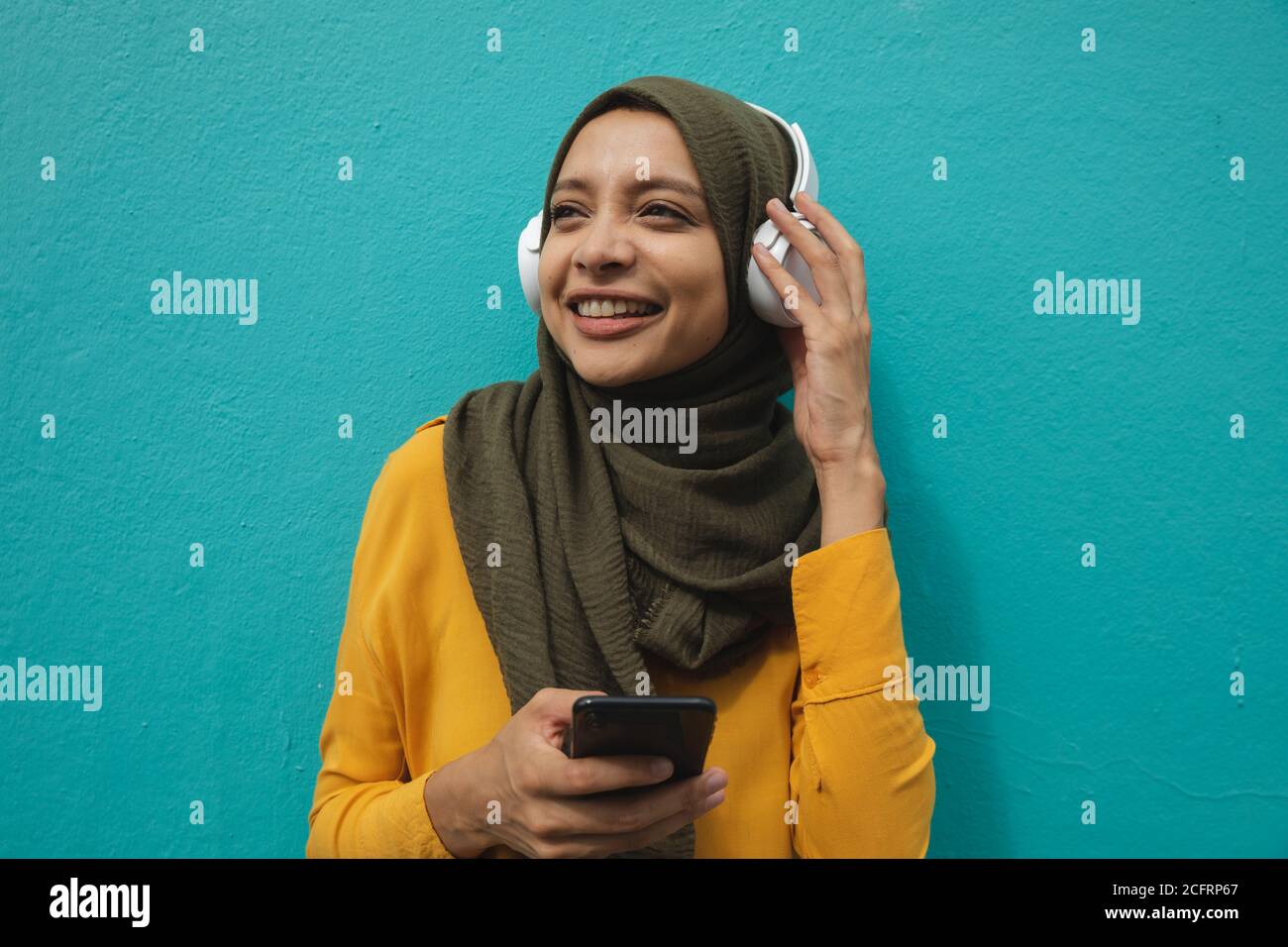 Frau in Hijab trägt Kopfhörer gegen eine blaue Wand Stockfoto