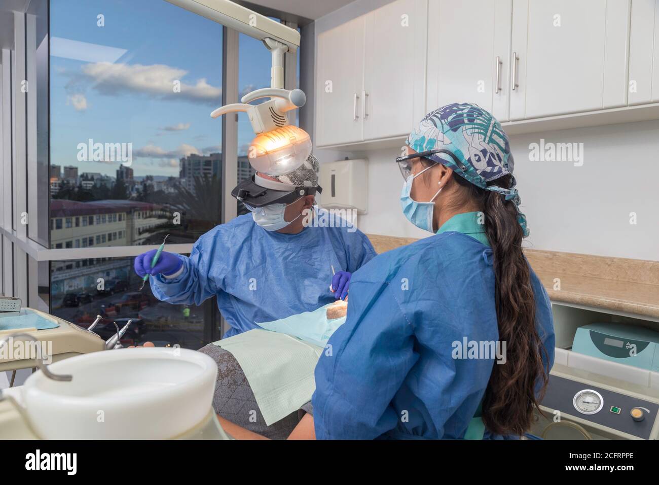 Zwei Zahnärzte mit Gesichtsmaske und Schutzmaßnahmen arbeiten auf Beratungsraum mit einem Patienten, Details Stockfoto
