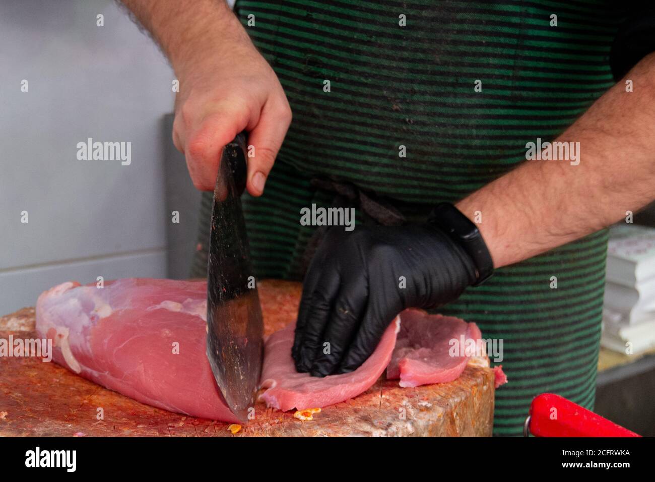 Metzger schneidet ein Stück Fleisch auf dem Holzbrett Und ein scharfes Messer in der Metzgerei Stockfoto