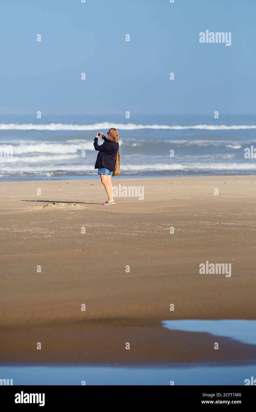 Frau, die den pazifik in Oregon mit ihrem Smartphone fotografiert, vertikal Stockfoto