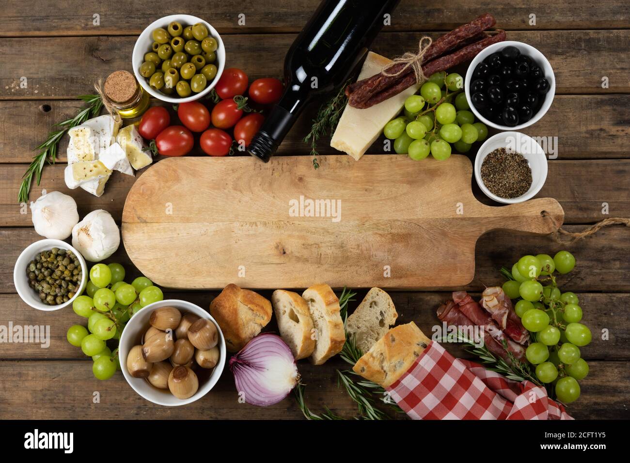 Blick auf ein Holzschneidebrett mit Brot, Käse, Wurst, Obst und Wein auf einer Holzfläche Stockfoto