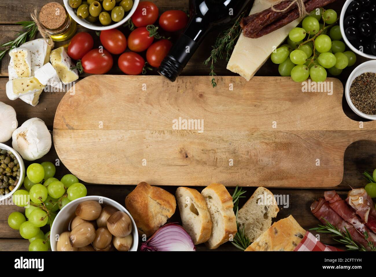 Blick auf ein Holzschneidebrett mit Brot, Käse, Wurst, Obst und Wein auf einer Holzfläche Stockfoto