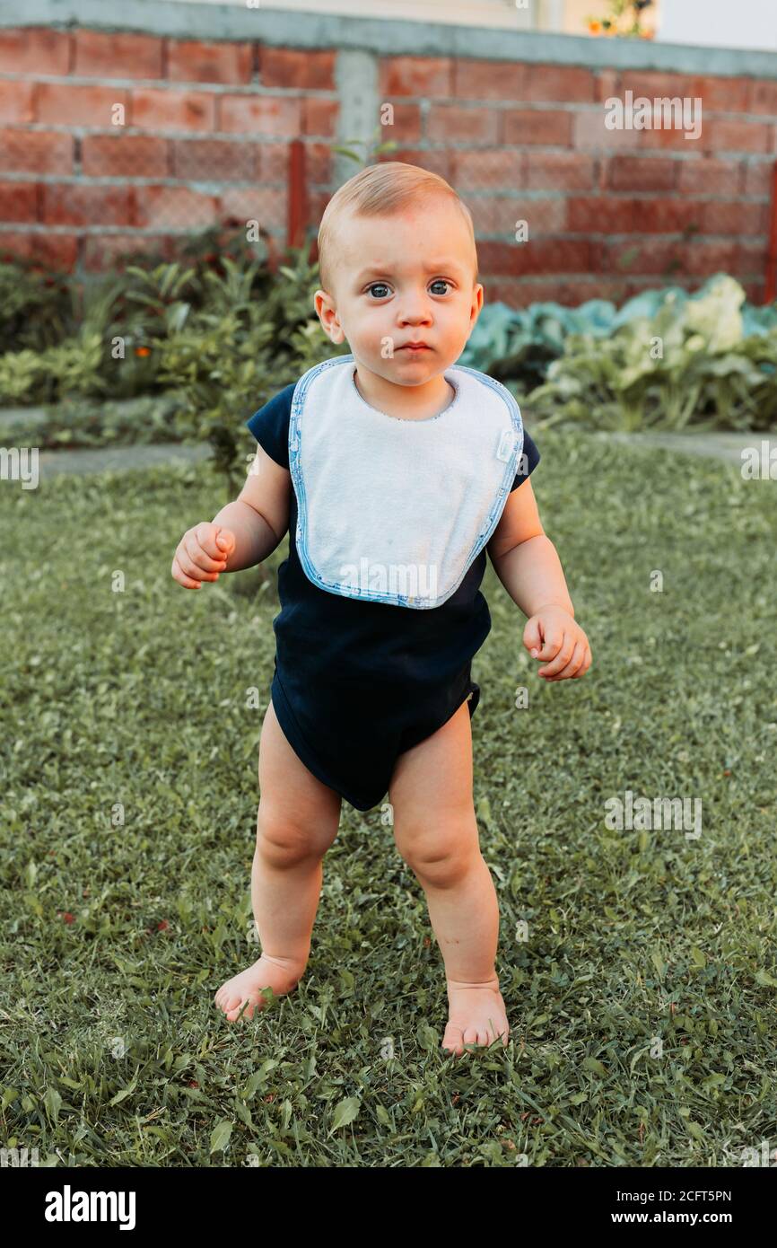 Liebenswert ein Jahr alten Jungen steht im Gras barfuß, hält sein Gleichgewicht, sieht verwirrt Stockfoto