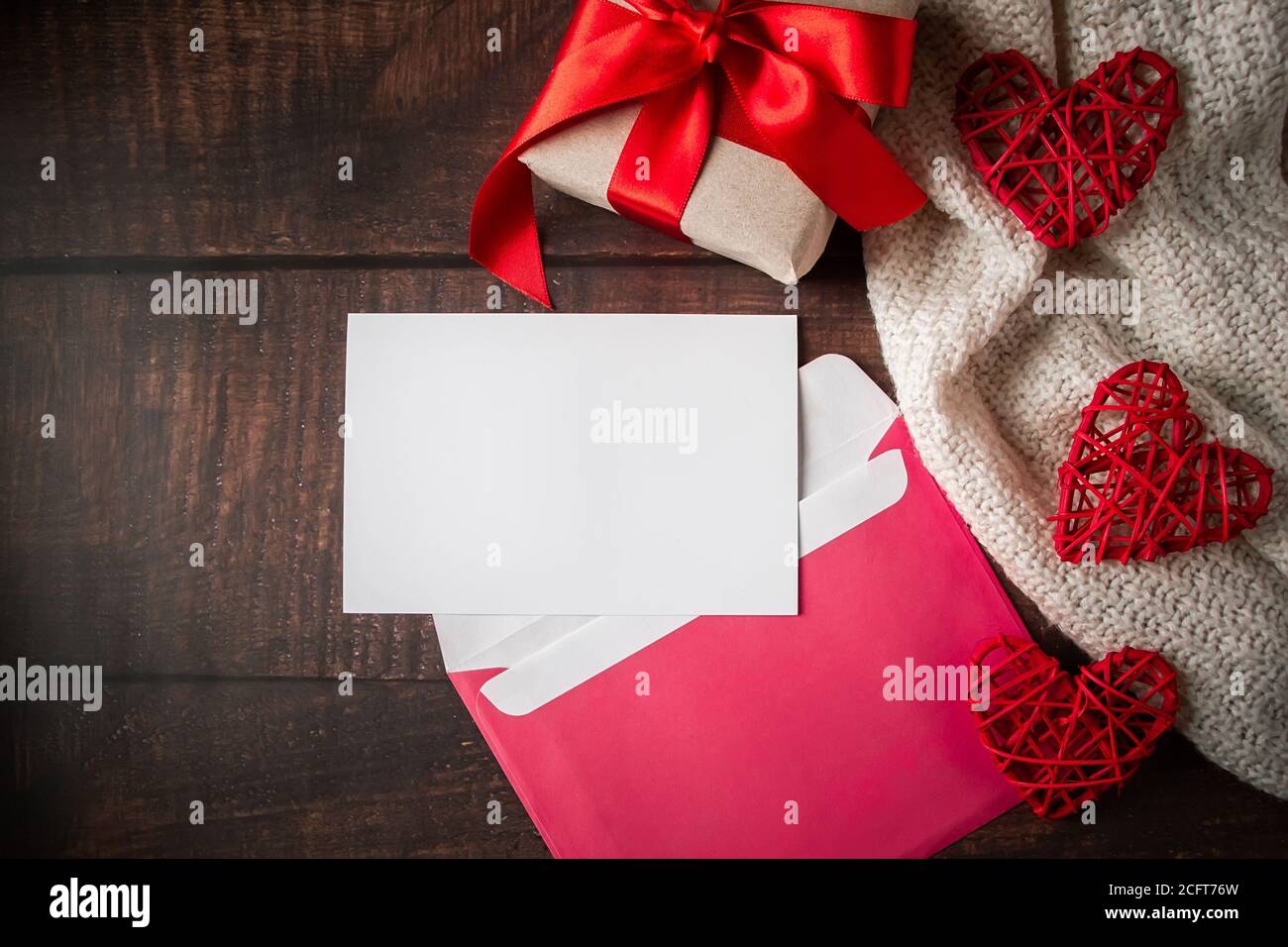 Umschlag und Grußkarte auf Holzhintergrund. Valentinstag Glückwunschbrief in einem rosa Umschlag. Geschenk und rote Herzen auf dem Hintergrund von Stockfoto