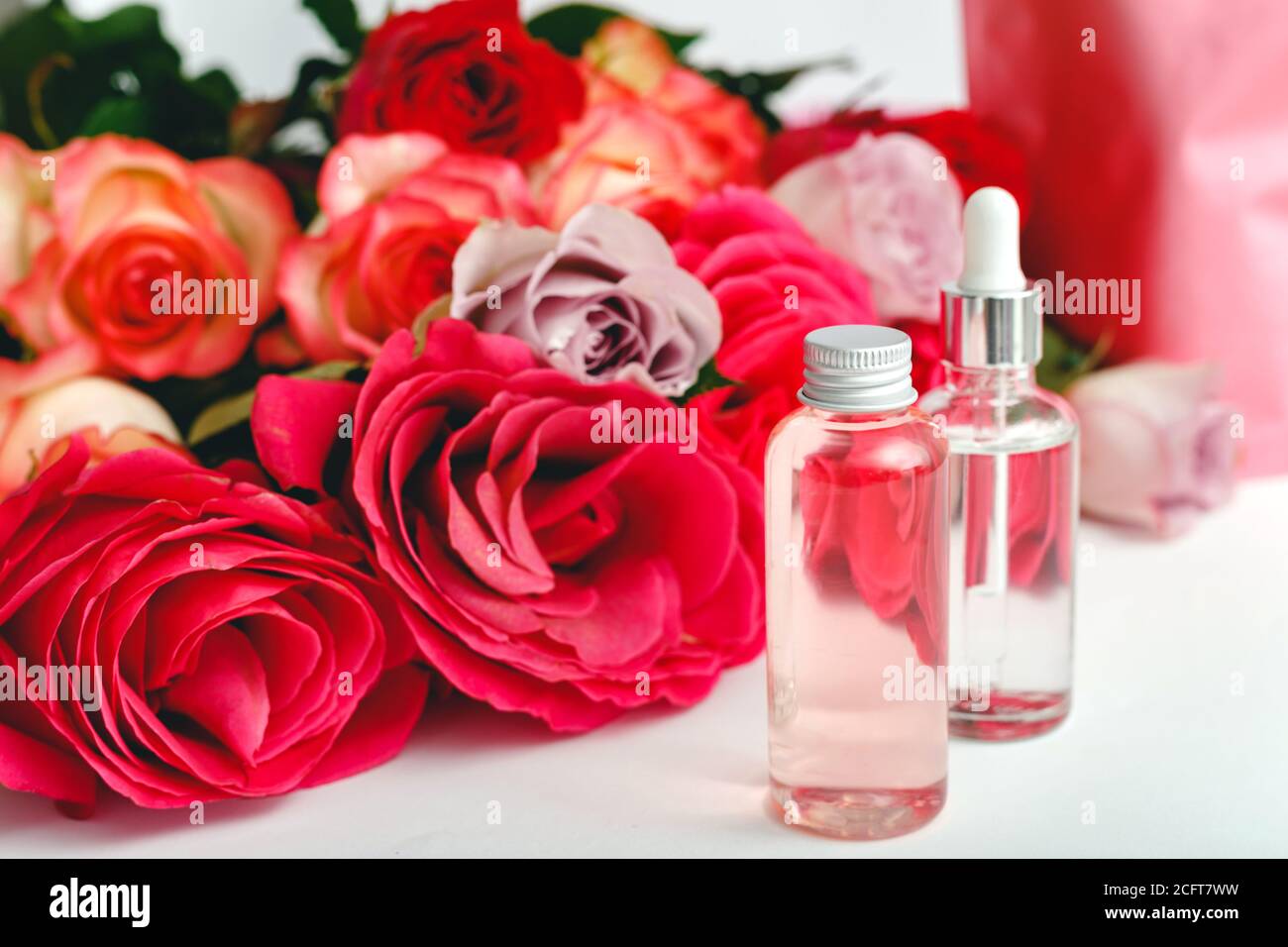 Glas Kosmetikflaschen, Serum, Seife, Öl auf weißem Tisch floralen Hintergrund. Blume rot rosa Rosen natürliche organische Schönheit Produkt. Spa, Hautpflege, Bad Stockfoto