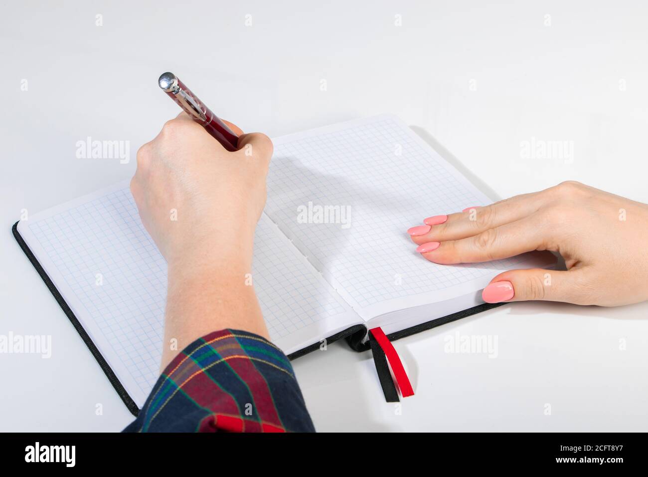 Die junge Frau hält einen Stift in der linken Hand und schreibt eine Notiz in ein leeres Notizbuch. Internationaler Tag Der Linken Stockfoto