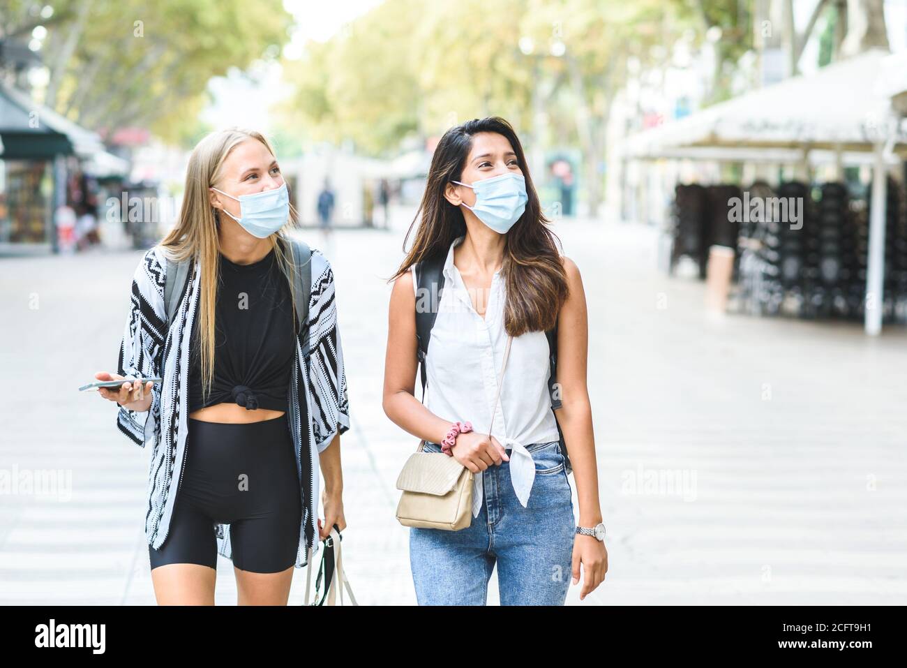 Zwei junge Touristen tragen blaue Schutzmasken und Kleidung Zwangloses Spazierengehen in den Straßen von Barcelona Stockfoto