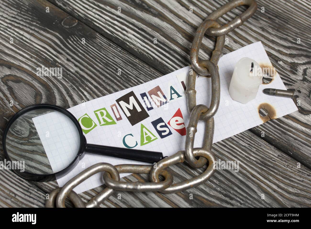 Die Phrase Criminal Case aus Buchstaben aus einer Zeitschrift geschnitten und auf einem Blatt Papier geklebt. In der Nähe liegt eine Metallkette, eine Lupe, eine kleine-ca Stockfoto