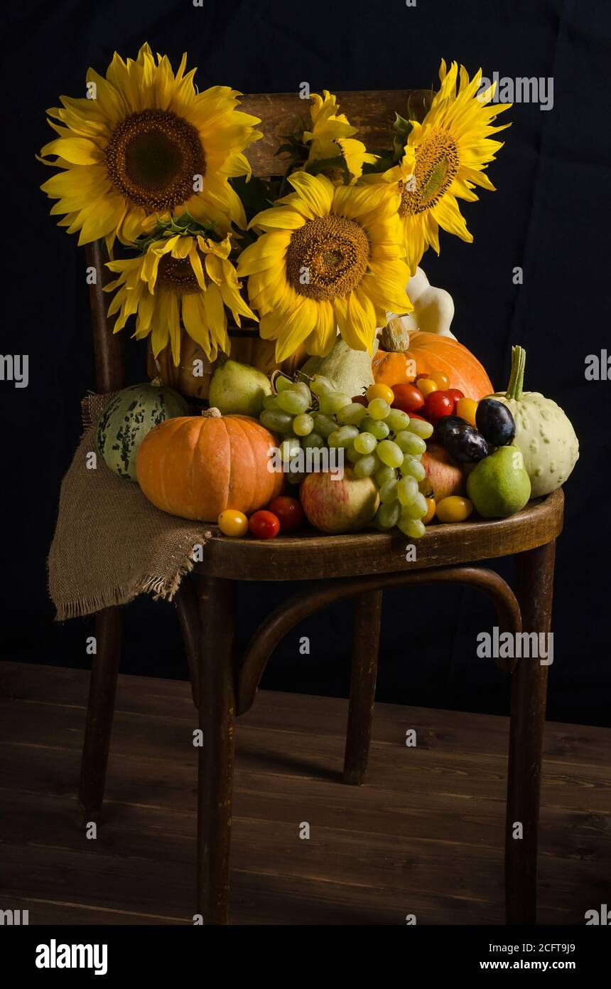 Stillleben mit Sonnenblumen aus Gemüse und Obst auf schwarzem Hintergrund im dunklen Stil. Erntedankfest und Ernte. Stockfoto