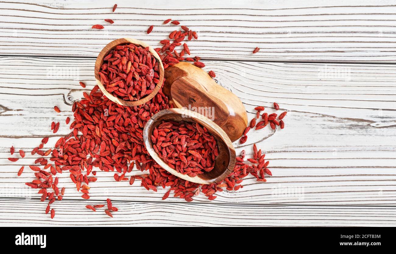 Getrocknete Goji Beeren in Holzschüsseln, verstreut über weißen Brettern Tisch unter, Blick von oben Stockfoto