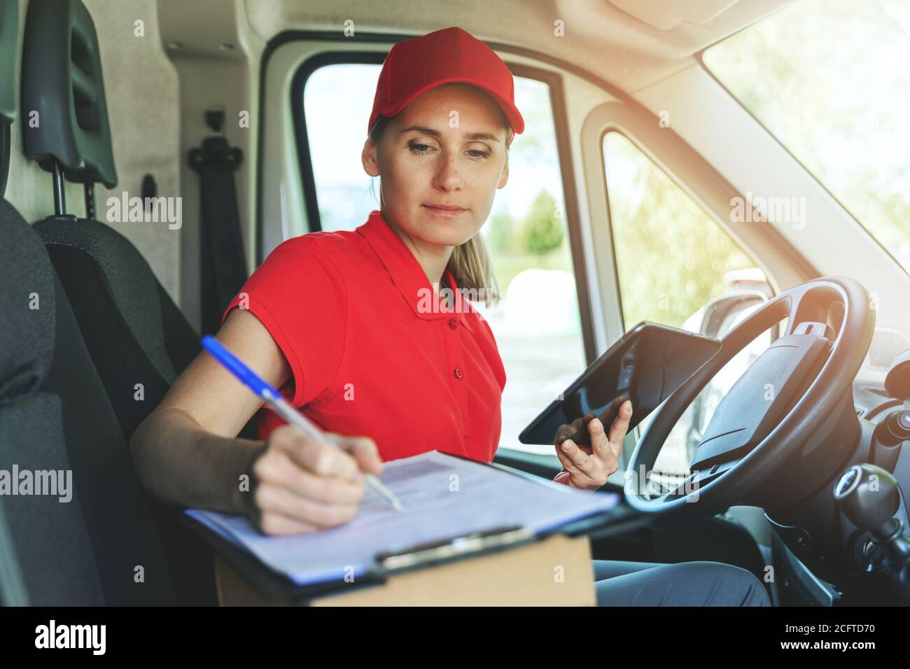 Lieferperson in roter Uniform sitzt im Lieferwagen und schreibt Dokumente in der Zwischenablage Stockfoto