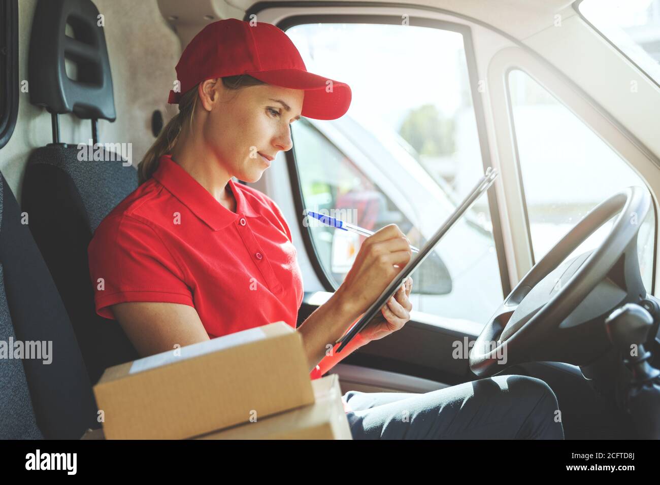 Lieferung Frau in roter Uniform sitzt in van und schriftlich Dokumente Stockfoto