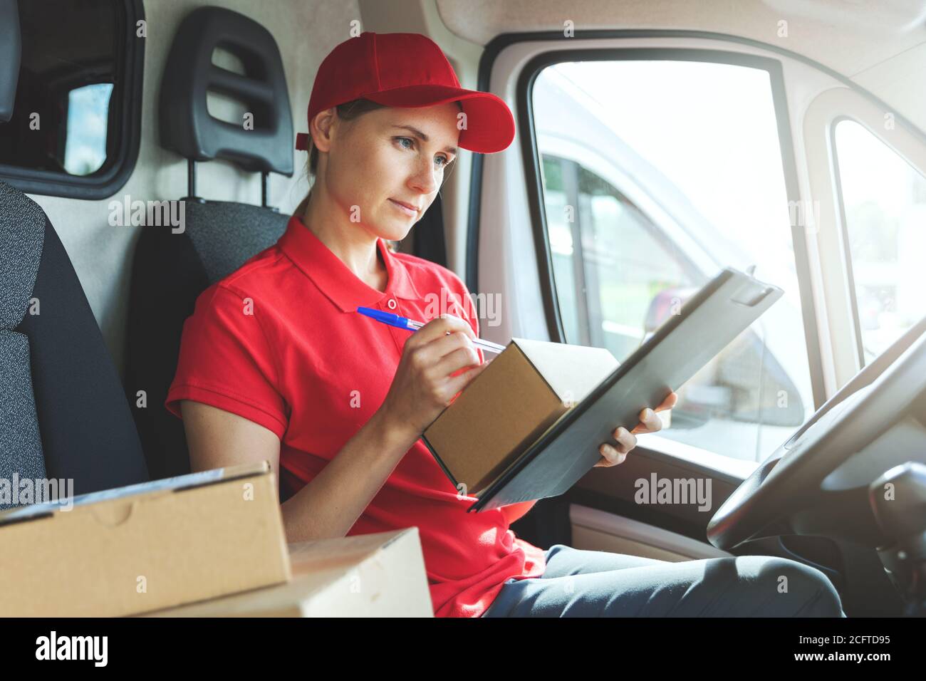 Lieferung Frau in roter Uniform sitzt in van und schriftlich Dokumente Stockfoto