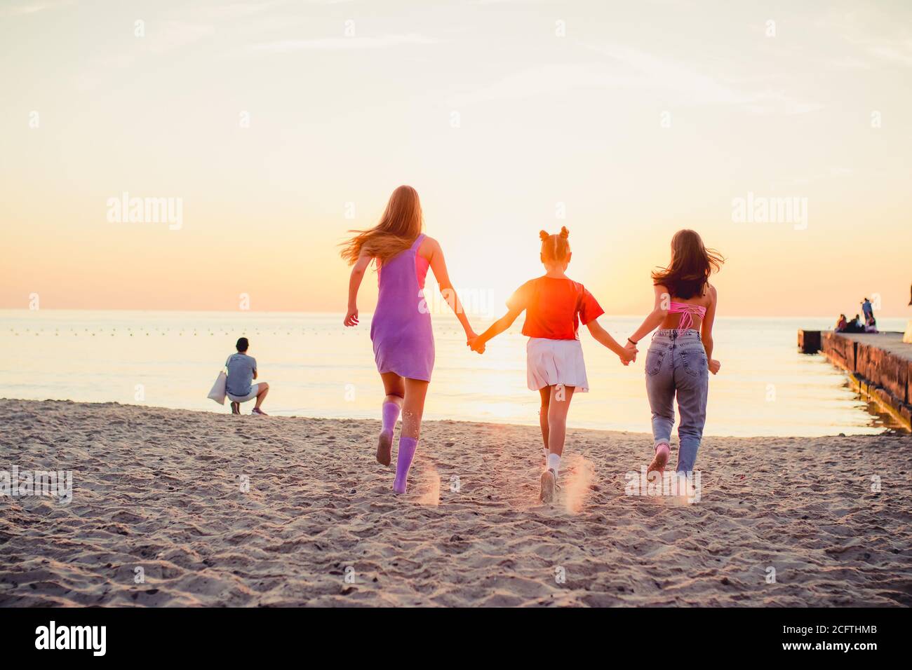 Drei junge Mädchen, die am Sandstrand entlang ins Meer laufen. 