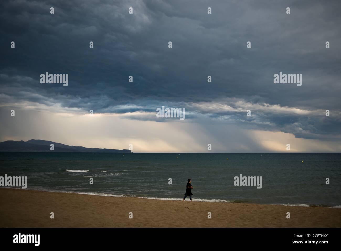 Sant Pere Pescador, Provinz Girona, Spanien. 6. Sep, 2020 - EINE Frau geht am Strand von Sant Pere Pescador, Nordspanien, spazieren, während Regensäulen am Horizont fallen. Das Ende der Sommerferien ist mit stürmischem Wetter gekommen. Quelle: Jordi Boixareu/Alamy Live News Stockfoto