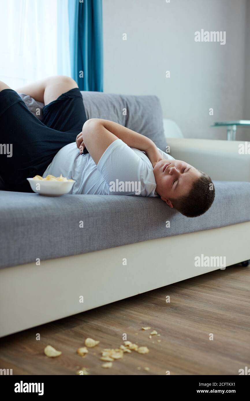 Überessen Fett Junge schlafen auf dem Sofa im Wohnzimmer, junge kaukasischen Teenager-Junge einschlafen, während er Fernsehen und Chips essen Stockfoto