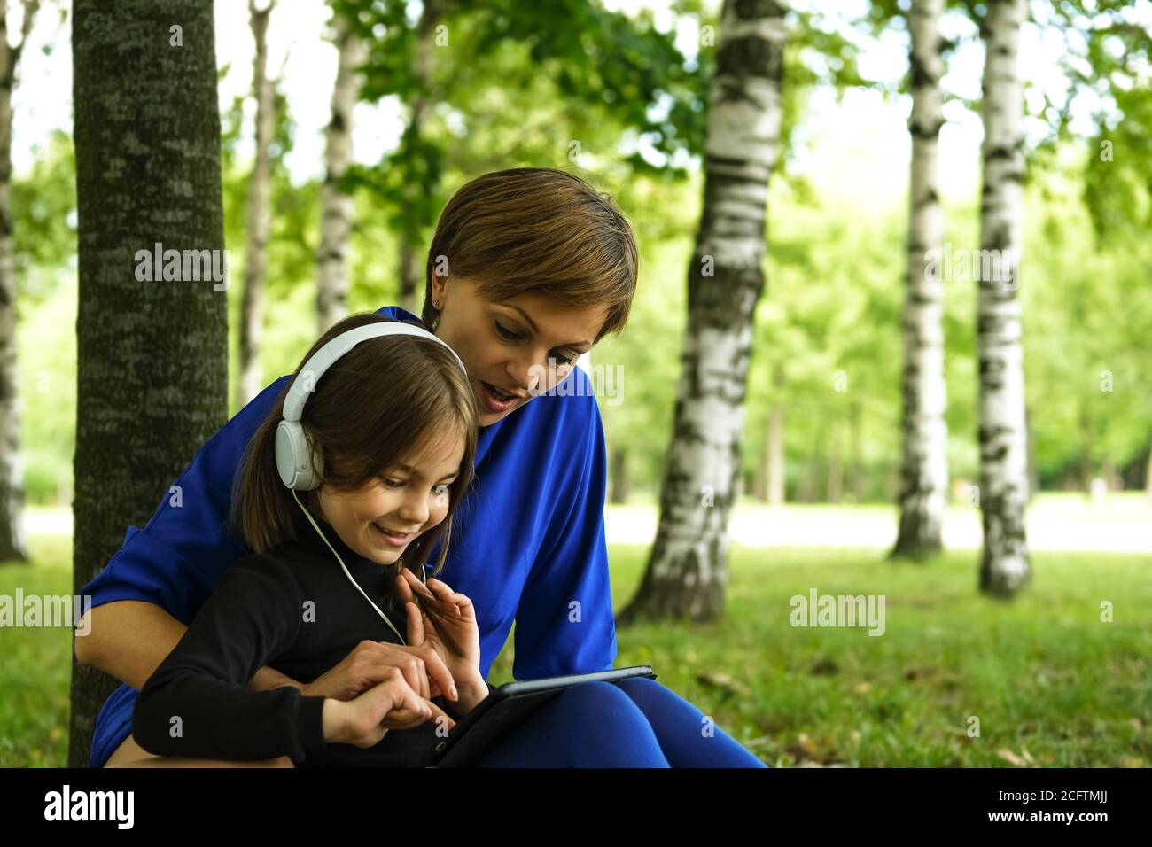 Mutter hilft ihrem Daightrer mit E-Education.Happy girl in weißen Kopfhörern mit digitalen Tablet-pc im Park. Fernlernkonzept. Resilienz, zurück zur Schule, neue Normalität. Stockfoto