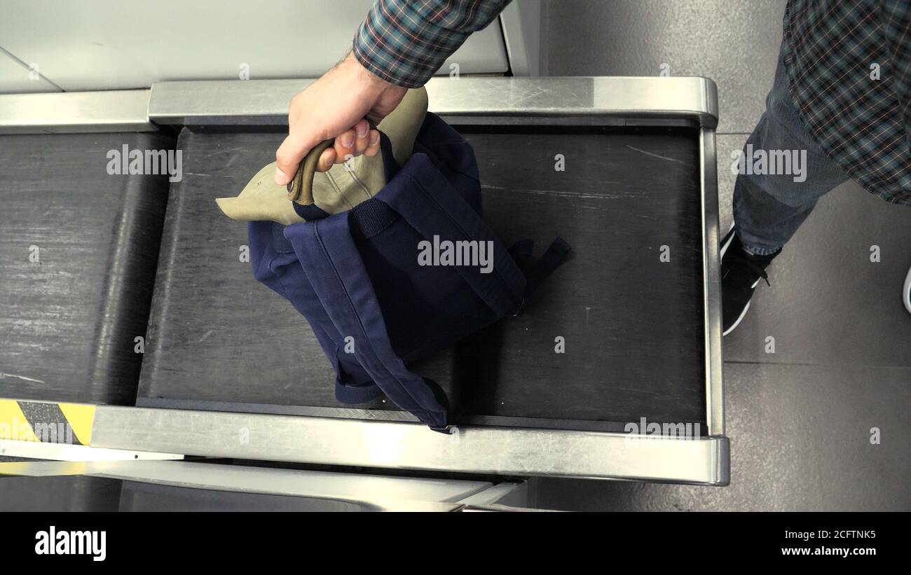 Die Hand eines Mannes mit einem Rucksack auf dem Gepäckförderband am Check-in-Schalter am Flughafen. Blauer Rückstand am Check-in-Schalter am Flughafen, gemessen am Stockfoto