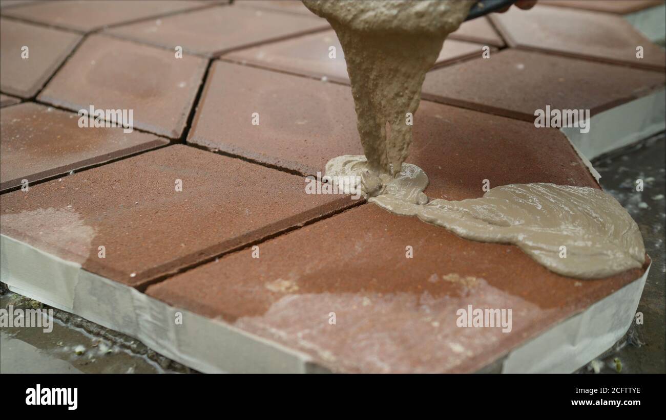 Füllen von Pflasterplatten mit einer Lösung auf der Straße. Der Bauherr füllt die Nähte zwischen den Pflasterplatten. Stockfoto