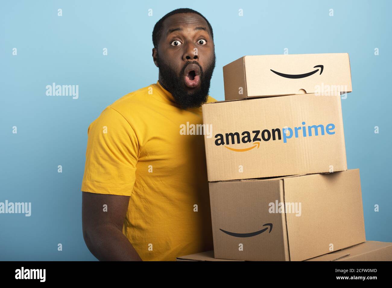 Überrascht Mann hält eine Menge von Amazon Prime-Pakete. Cyanfarbener Hintergrund Stockfoto