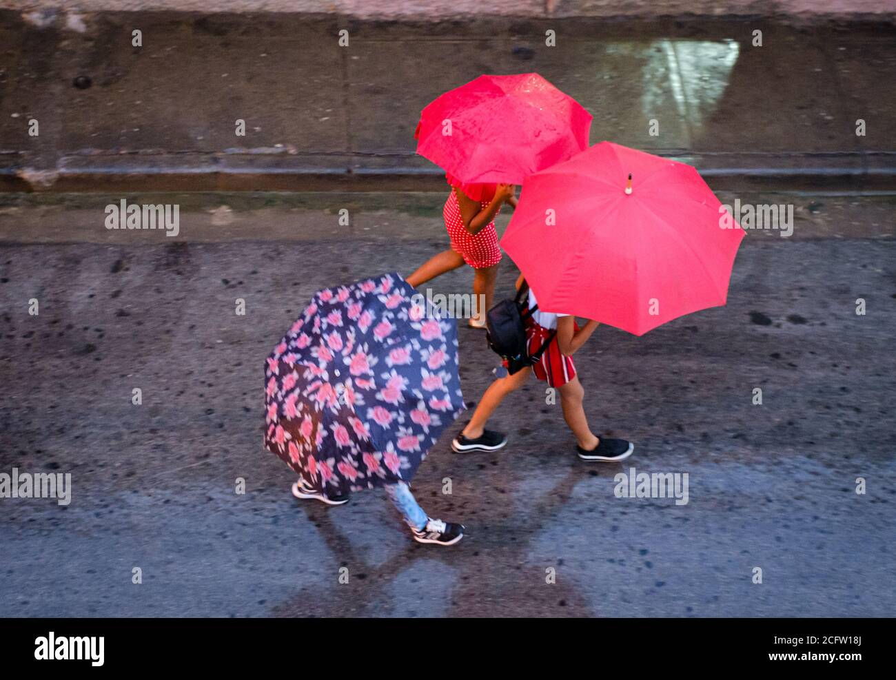 SANTIAGO DE CUBA, KUBA - CA. JANUAR 2020: Fußgänger, die an einem regnerischen Tag in Santiago de Cuba spazieren. Stockfoto