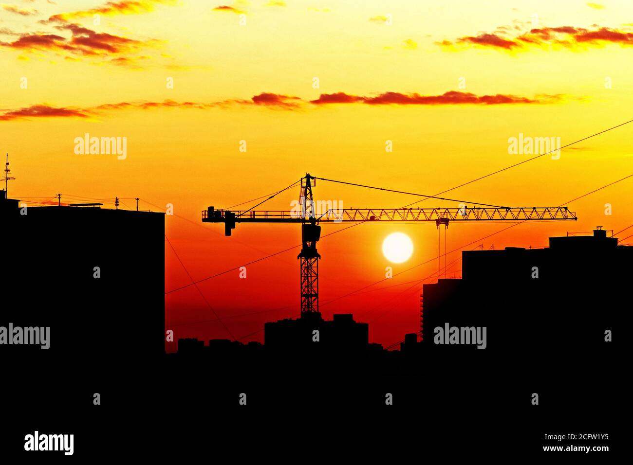 Silhouetten von Häusern und Baukran gegen untergehende Sonne, Skyline der Stadt bei Sonnenuntergang Stockfoto