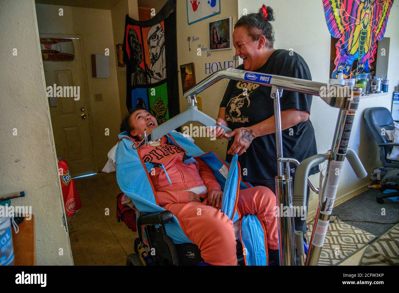 Sacramento, Kalifornien, USA. Februar 2020. FELICIA BRENT-VELASQUEZ teilt einen Lichtmoment mit ihrer Mutter FELICIA CLARK, während sie in ihrem Aufzug zu ihrem Rollstuhl in ihrem Haus in Sacramento gehisst wird. Clark hatte mehrere Stunden damit verbracht, sie anzuziehen, ihr Haar zu stylen, sie zu waschen, sie zu füttern, die Öffnung in ihrer Luftröhre zu saugen, als sie blockiert wurde, und dann sie in Decken gebündelt, um draußen zu gehen, um gegen das Kinderheim von Sacramento zu protestieren, wo sie einst lebte. Quelle: Renee C. Byer/Sacramento Bee/ZUMA Wire/Alamy Live News Stockfoto