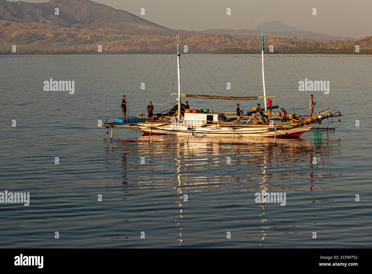 Ein Fischer steht am Bug eines Jukung-Außerbordboots vor der Küste von Lembata, Indonesien, während seine Kameraden Netze und Ausrüstung an Deck handhaben. Stockfoto