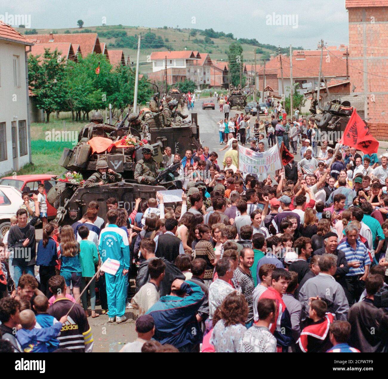 1999 - Ethenic Albaner versammeln sich in den Straßen für eine Parade statt die amerikanischen Streitkräfte im Kosovo Dorf Koretin zu ehren. Marines an Bord ihrer LAV-25, Leichte gepanzerte Fahrzeuge sind entlang der Straße Seite gesehen. Stockfoto