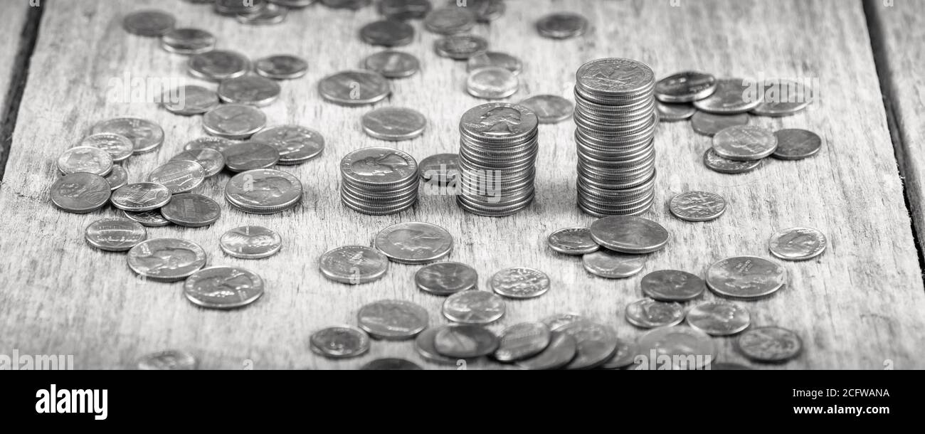 Stapel von Vierteln auf einem alten Holztisch inmitten verstreut Münzen in Schwarz und Weiß / Investitionswachstumskonzept Stockfoto