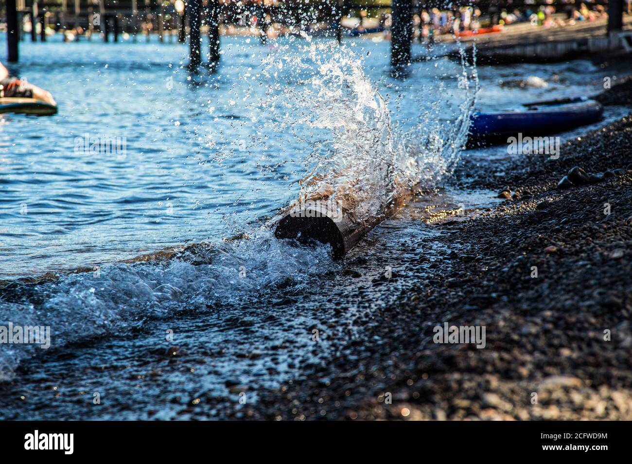 Wasser spritzt über einen Baumstamm, während die Strömung auf Kieselsteinen bricht Ufer des Lake Tahoe in Tahoe City Beach Park Association Pier Stockfoto