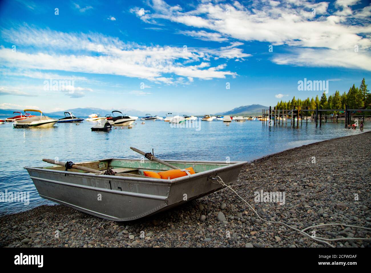 Altes Ruderboot aus Metall mit Rudern und orangefarbener Schwimmweste, hochgezogen auf felsigen Ballen am Rande des Lake Tahoe, Marina-Boote und Pier im Hintergrund Stockfoto