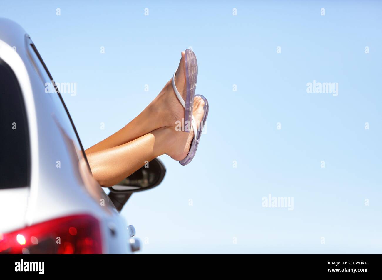 Sommer Roadtrip Auto Urlaub Spaß. Frau Beine aus dem Auto Fenster in blauen Himmel Hintergrund. Sorglos, Freiheit, Roadtrip und Urlaub kopieren Platz Stockfoto