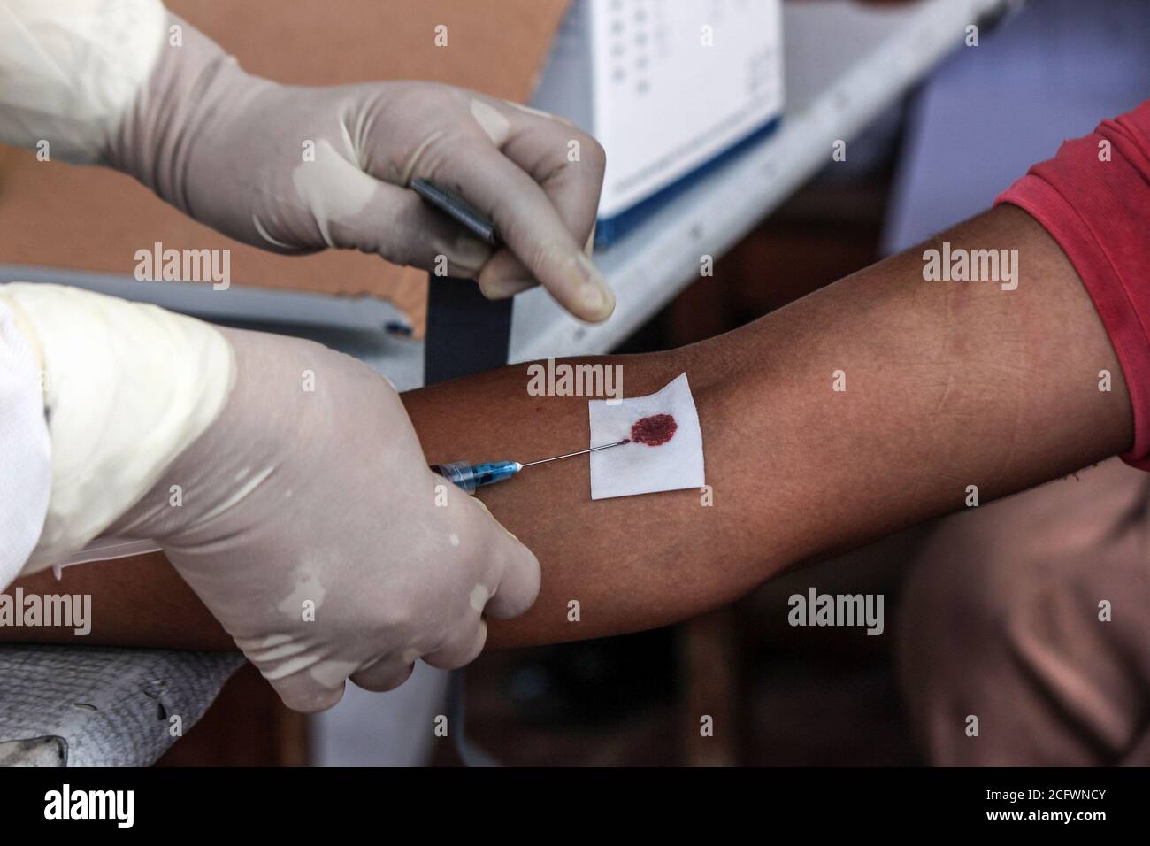 Lhokseumawe, Indonesien. September 2020. Ein Polizist, der einen ethnischen Rohingya-Flüchtling in einem provisorischen Unterschlupf untersucht, nimmt Blut in einem Schutzanzug (PSA).Fast 300 ethnische Rohingya-Muslime sind in den Gewässern des Aceh-Meeres gestrandet. Bestehend aus Erwachsenen und Kindern, die aufgrund von Austrocknung und Hunger schwach sind, nachdem sie auf hoher See beeinflusst wurden. Kredit: SOPA Images Limited/Alamy Live Nachrichten Stockfoto