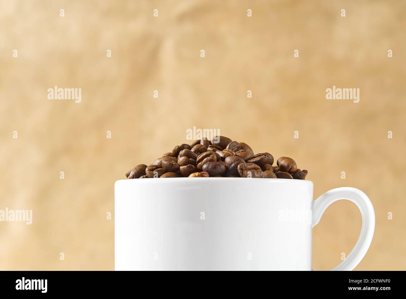 Internationaler Tag des Kaffees Konzept. Nahaufnahme weiße Kaffeetasse voller Kaffeebohnen auf beigem Hintergrund. Stockfoto