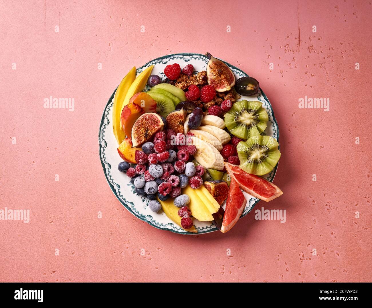 Verschiedene geschnittene Früchte auf Vintage-Teller. Draufsicht auf Mango, Kiwi-Früchte, Feigen, Trauben, Bananen, Himbeeren und Heidelbeeren auf rosa Hintergrund. Stockfoto
