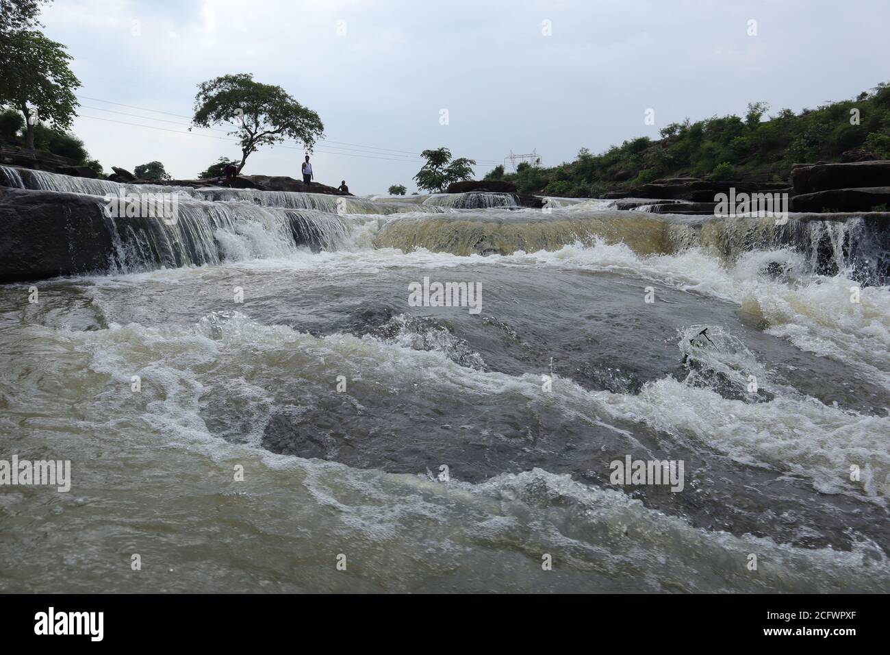 Bokeh-Aufnahme eines fließenden Wasserfalls mit selektivem Fokus und Baumhintergrund. Kleine Kinder baden im gefährlichen Wasserfall in Mirzapur, Indien w Stockfoto
