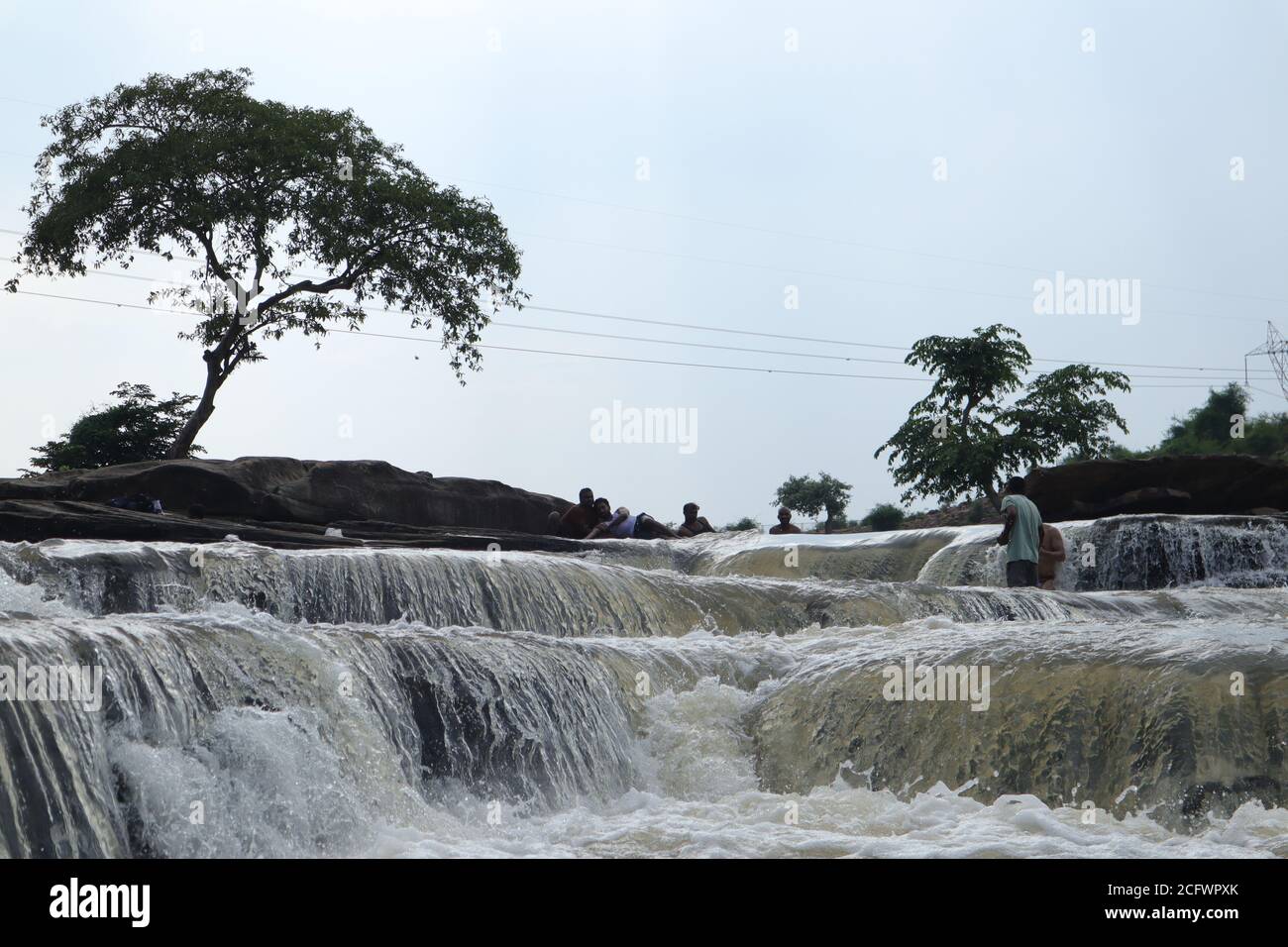 Bokeh-Aufnahme eines fließenden Wasserfalls mit selektivem Fokus und Baumhintergrund. Kleine Kinder baden im gefährlichen Wasserfall in Mirzapur, Indien w Stockfoto
