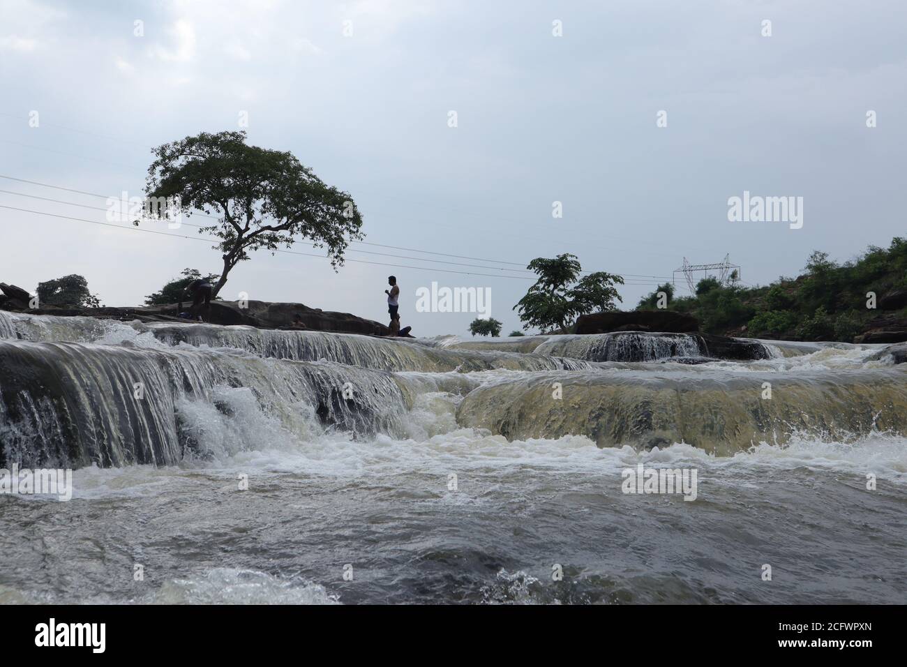 Bokeh-Aufnahme eines fließenden Wasserfalls mit selektivem Fokus und Baumhintergrund. Kleine Kinder baden im gefährlichen Wasserfall in Mirzapur, Indien w Stockfoto