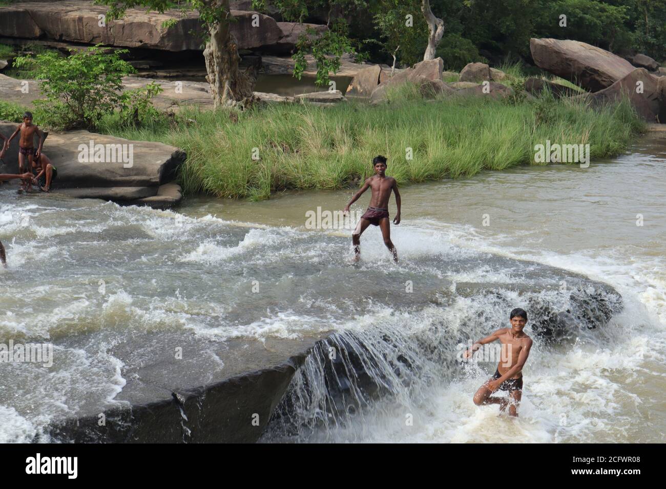 Bokeh-Aufnahme eines fließenden Wasserfalls mit selektivem Fokus und Baumhintergrund. Kleine Kinder baden im gefährlichen Wasserfall in Mirzapur, Indien w Stockfoto