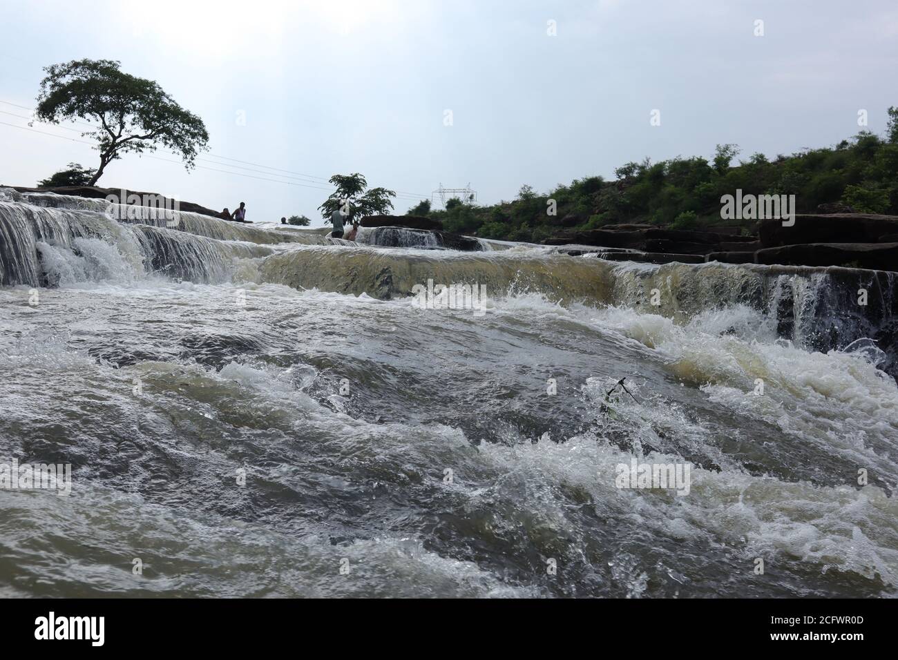 Bokeh-Aufnahme eines fließenden Wasserfalls mit selektivem Fokus und Baumhintergrund. Kleine Kinder baden im gefährlichen Wasserfall in Mirzapur, Indien w Stockfoto