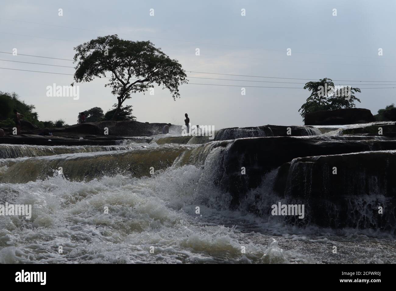 Bokeh-Aufnahme eines fließenden Wasserfalls mit selektivem Fokus und Baumhintergrund. Kleine Kinder baden im gefährlichen Wasserfall in Mirzapur, Indien w Stockfoto