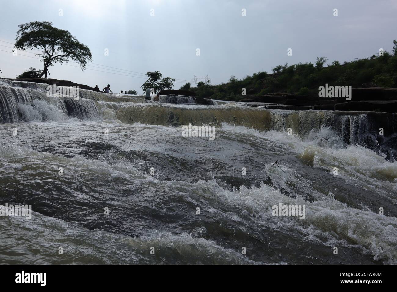 Bokeh-Aufnahme eines fließenden Wasserfalls mit selektivem Fokus und Baumhintergrund. Kleine Kinder baden im gefährlichen Wasserfall in Mirzapur, Indien w Stockfoto