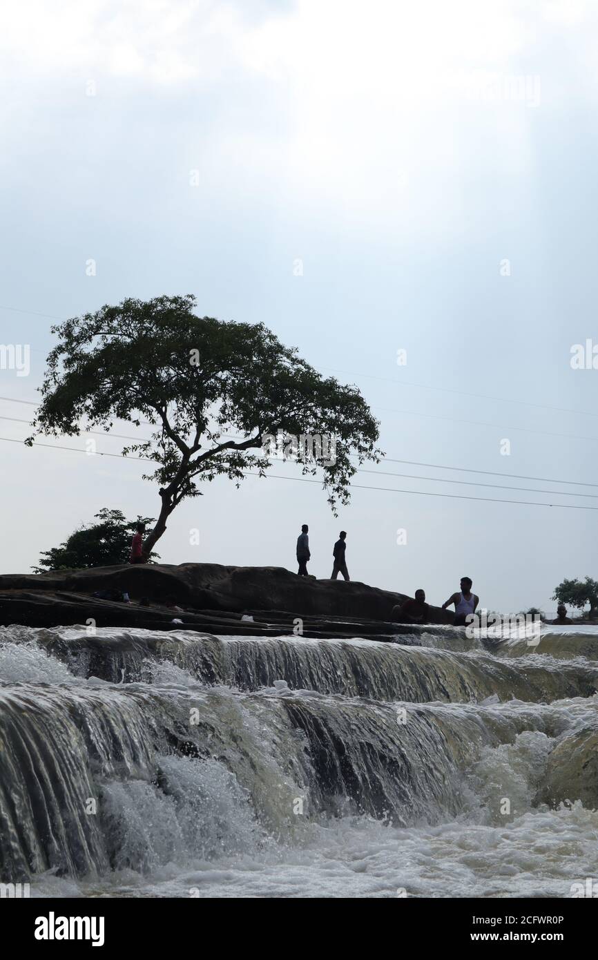 Bokeh-Aufnahme eines fließenden Wasserfalls mit selektivem Fokus und Baumhintergrund. Kleine Kinder baden im gefährlichen Wasserfall in Mirzapur, Indien w Stockfoto