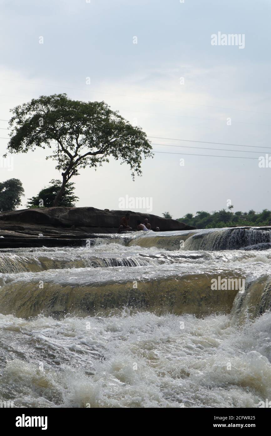 Bokeh-Aufnahme eines fließenden Wasserfalls mit selektivem Fokus und Baumhintergrund. Kleine Kinder baden im gefährlichen Wasserfall in Mirzapur, Indien w Stockfoto