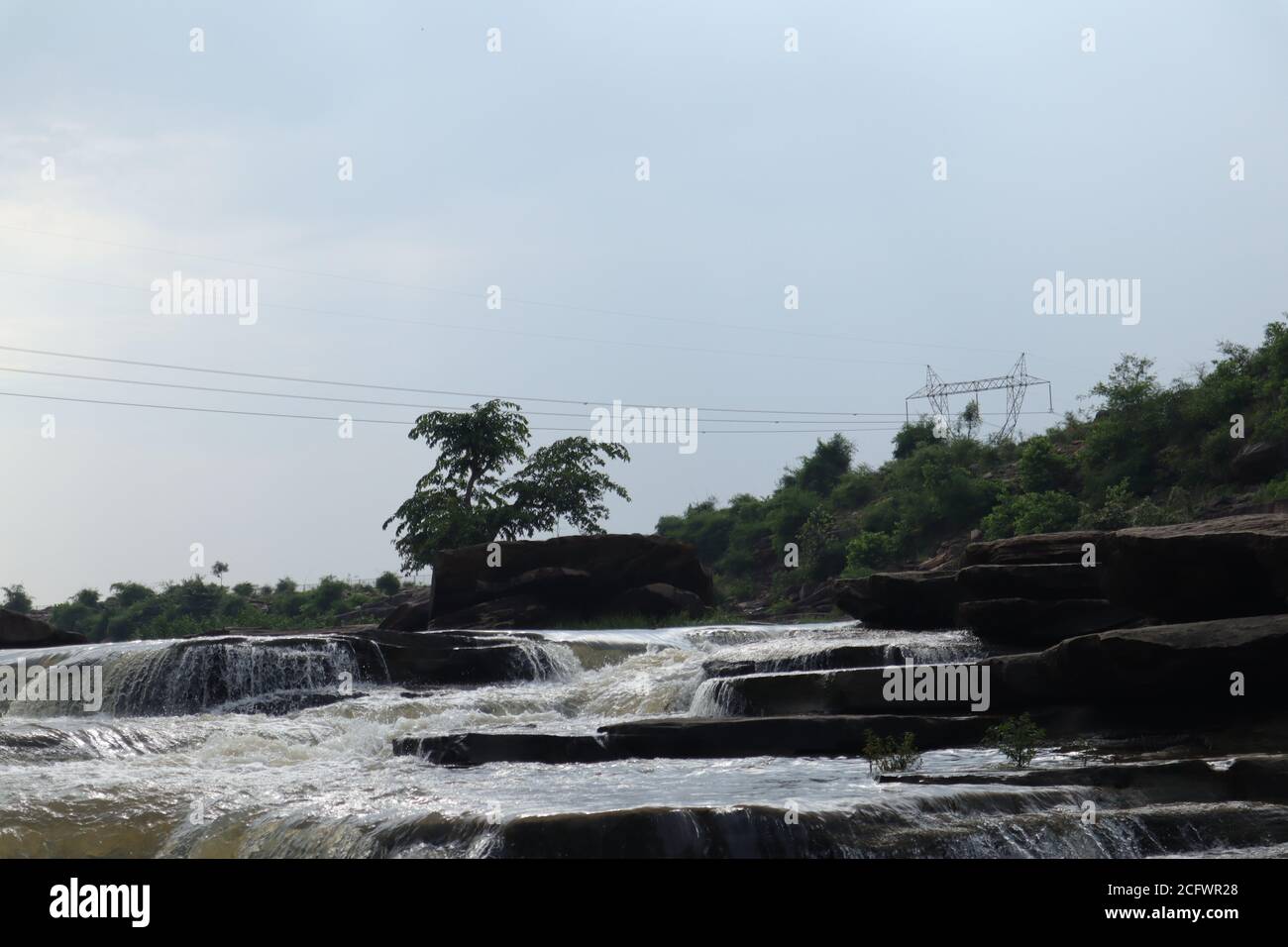 Bokeh-Aufnahme eines fließenden Wasserfalls mit selektivem Fokus und Baumhintergrund. Kleine Kinder baden im gefährlichen Wasserfall in Mirzapur, Indien w Stockfoto